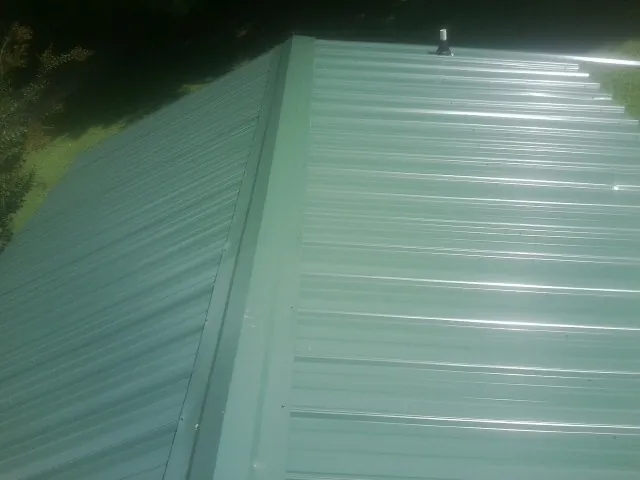 New green metal panels meeting at the ridge of a roof — Flat Roof Repair work by our crew in Leland